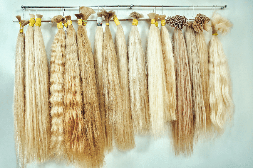 Various shades and textures of blonde hair extensions displayed on a metal rack.