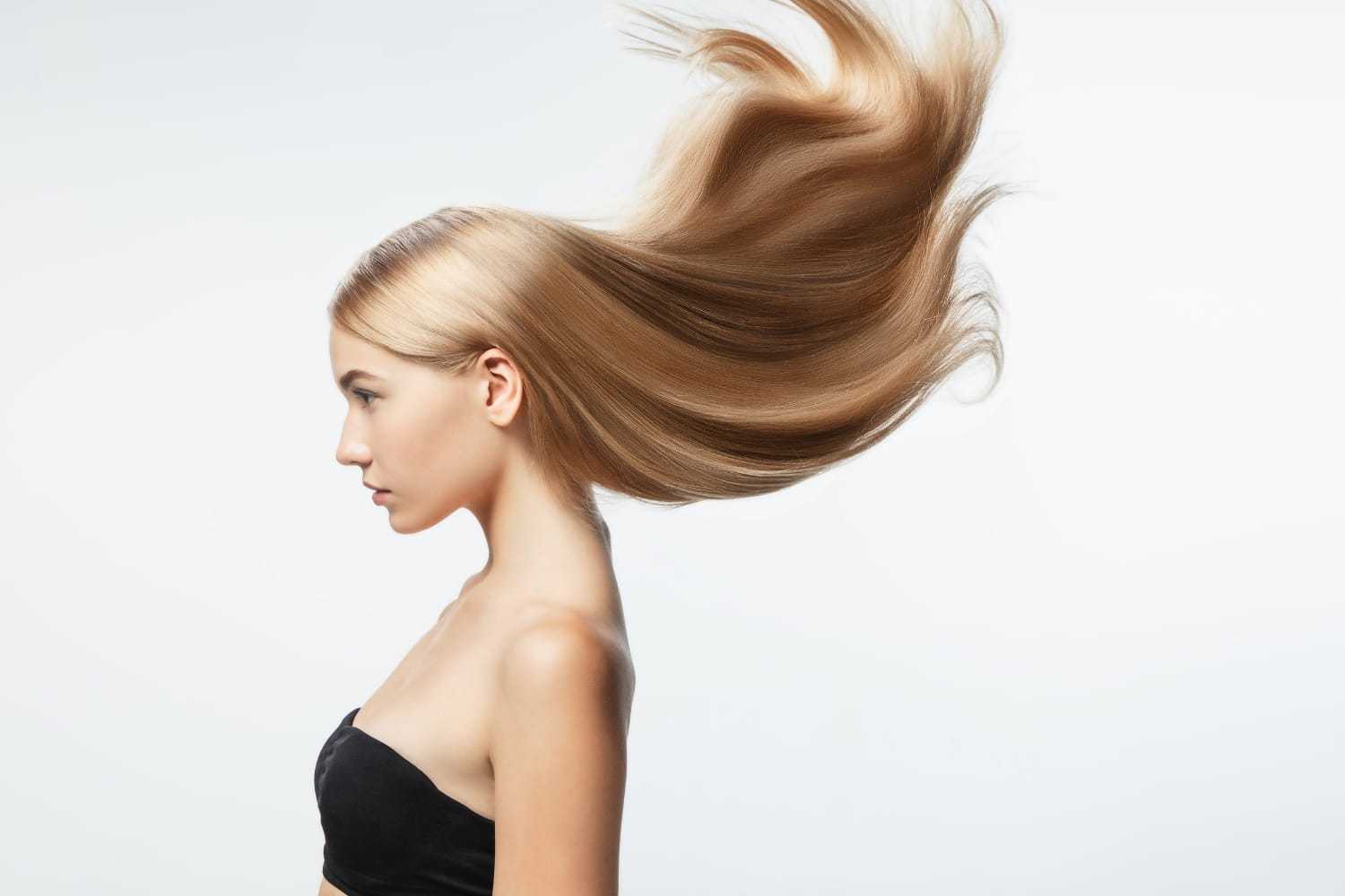 Side profile of a woman with long, flowing blonde hair in a black strapless top against a white background.