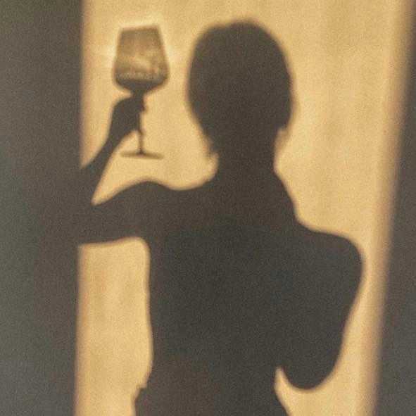 Shadow of a person holding a wine glass against a beige wall.